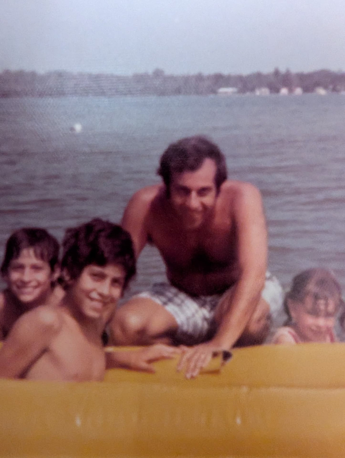 Dr. Rosey and his family swimming in a lake all gathered on an inflatable floating platform